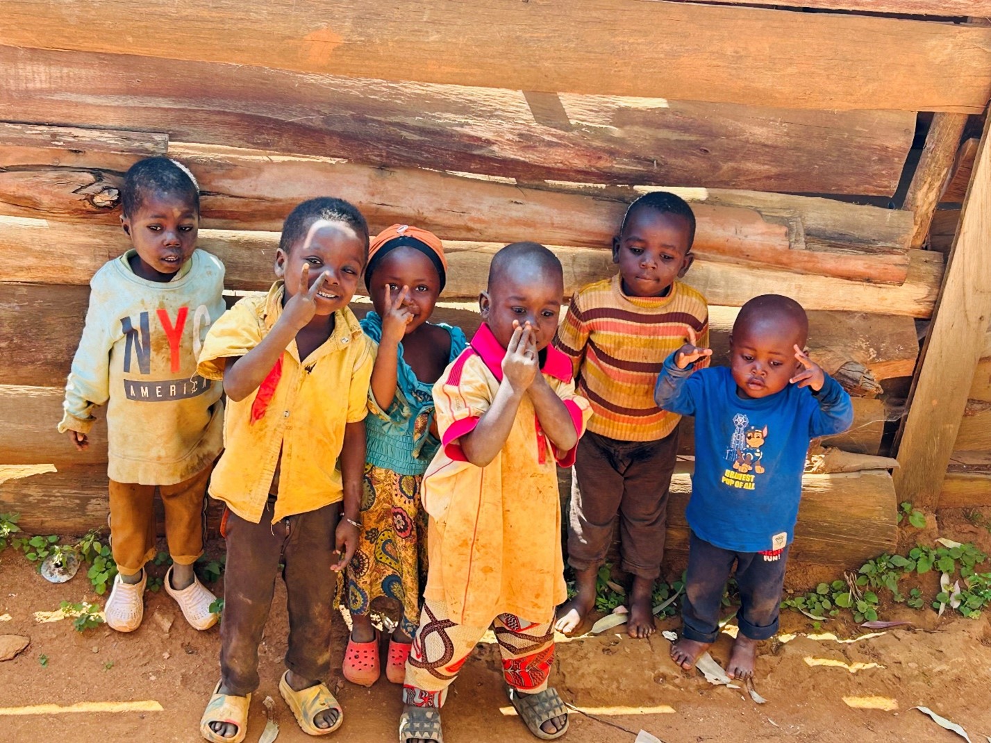 Eine Gruppe von fröhlichen kleinen Kindern mit brauner Hautfarbe steht vor einer Wand aus Holz